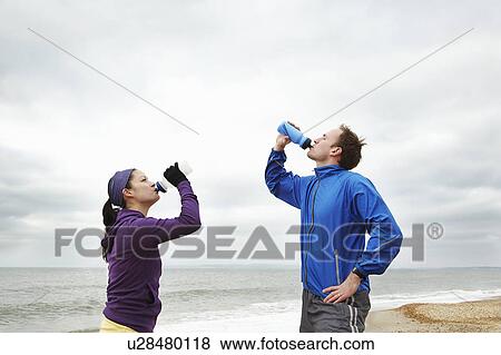 Couple drinking after exercise on beach View Large Photo Image Stock Photo - Couple drinking after exercise on beach. Fotosearch
