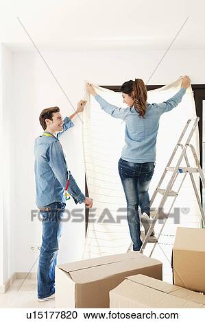 Stock Image - Couple hanging curtain in new home. Fotosearch