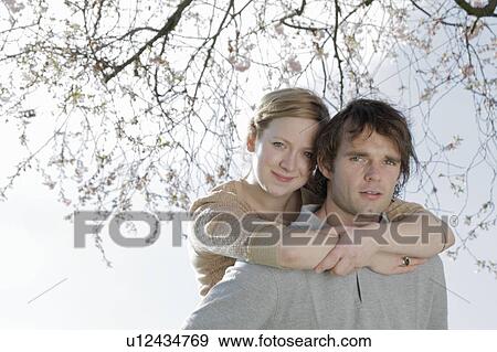 Stock Photo - Couple hugging under cherry blossom tree. Fotosearch