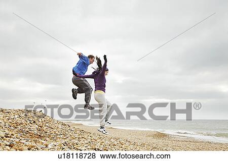 Couple jumping on beach on cloudy day View Large Photo Image Stock Photo - Couple jumping on beach on cloudy day. Fotosearch