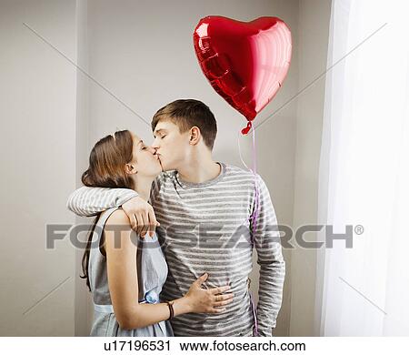 Stock Image - Couple kissing, holding heart balloon. Fotosearch