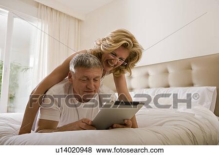 Couple looking at tablet computer in bed View Large Photo Image Stock Photo - Couple looking at tablet computer in bed. Fotosearch