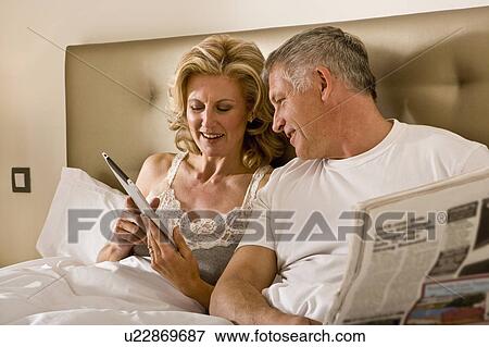 Couple looking at tablet computer in bed View Large Photo Image Stock Photo - Couple looking at tablet computer in bed. Fotosearch