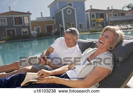 Couple on sunbeds laughing by pool View Large Photo Image Stock Photo - Couple on sunbeds laughing by pool. Fotosearch