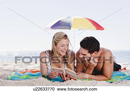 Stock Image - Couple reading book together on beach. Fotosearch