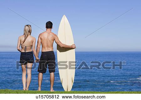Couple standing with surfboard by ocean View Large Photo Image Stock Image - Couple standing with surfboard by ocean. Fotosearch