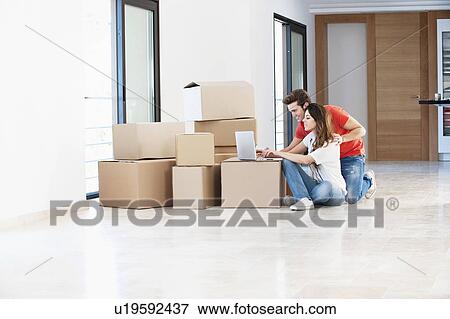Couple using laptop in new home View Large Photo Image Stock Photo - Couple using laptop in new home. Fotosearch