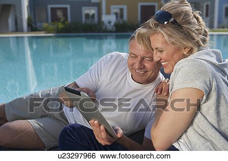 Stock Photograph - Couple using tablet computer by pool. Fotosearch