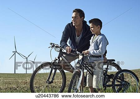 Stock Photograph - Father and son with bikes by a windfarm. Fotosearch
