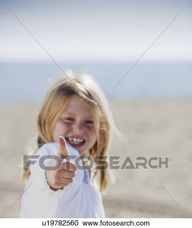 Stock Image - Girl at beach with thumb up to camera. Fotosearch