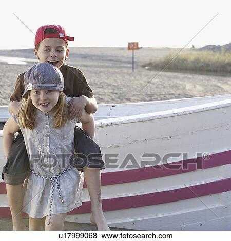 Stock Photo - Girl giving piggyback to boy by boat. Fotosearch