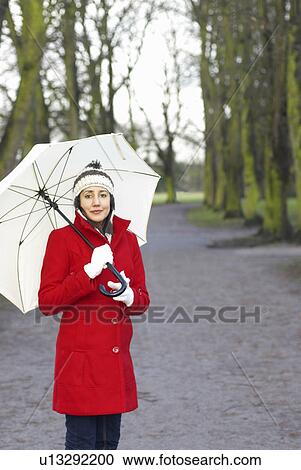 Stock Image - Girl in red jacket with brolley in park. Fotosearch