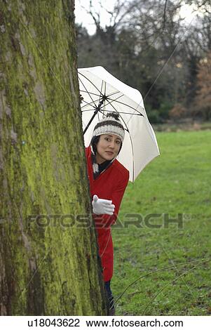 Stock Image - Girl in red jacket with brolley in park. Fotosearch