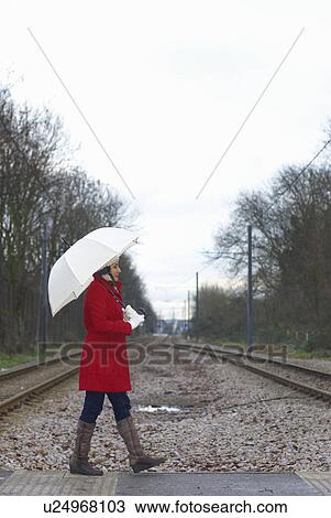 Stock Image - Girl in red jacket with brolley in park. Fotosearch