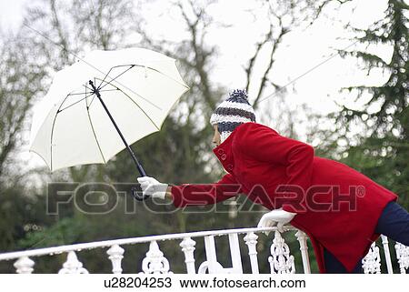 Stock Image - Girl in red jacket with brolley in park. Fotosearch