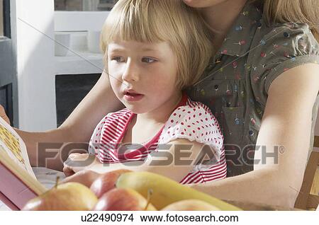 Picture - girl on mothers lap reading book. Fotosearch