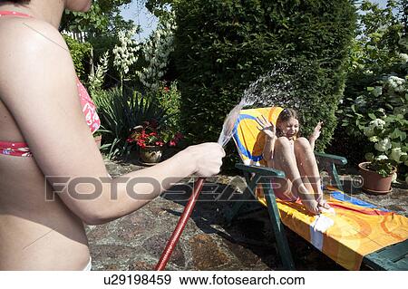 Girl sprays water on sister View Large Photo Image Stock Photo - Girl sprays water on sister. Fotosearch