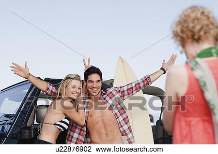 Stock Image - Girl taking picture of couple by jeep. Fotosearch