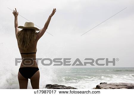 Stock Photo - Girl with arms up in front of ocean, water splashing. Fotosearch