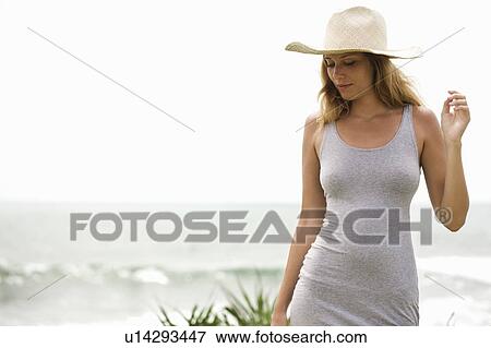 Stock Photo - Girl with straw hat in grey dress in front of ocean. Fotosearch
