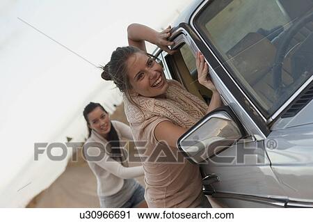 Stock Image - Girls pushing car. Fotosearch