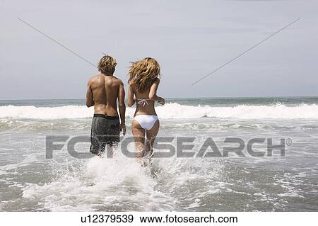 Stock Photo - Guy and girl running in water on beach. Fotosearch