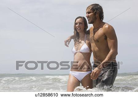 Stock Image - Guy and girl walking arm in arm in water. Fotosearch