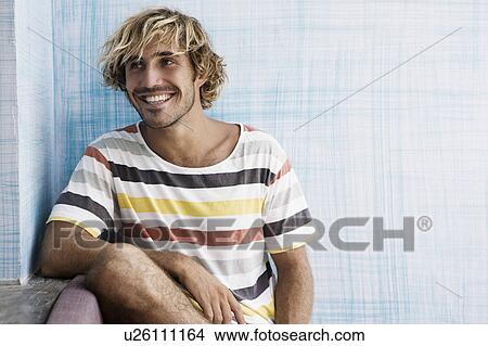 Guy sitting up against blue wall, looking to the side, laughing View Large Photo Image Picture - Guy sitting up against blue wall, looking to the side, laughing. Fotosearch