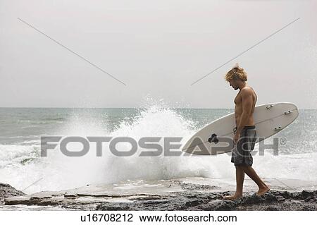 Guy walking on cliff with surfboard ocean behind him View Large Photo Image Stock Image - Guy walking on cliff with surfboard ocean behind him. Fotosearch