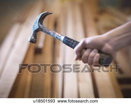 Stock Image - Hand holding hammer next to timber. Fotosearch
