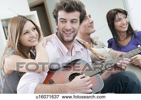 Stock Photo - Happy friends playing guitar together. Fotosearch