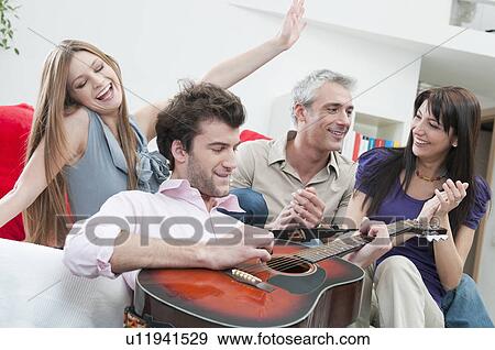 Stock Photo - Joyful friends playing guitar at home. Fotosearch
