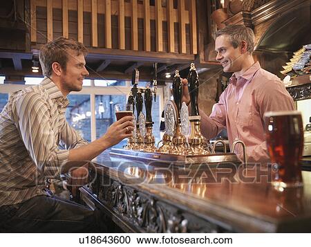 Stock Image - Landlord and customer in English pub. Fotosearch