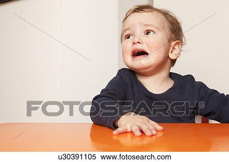 Stock Photography - Little boy sitting on table crying. Fotosearch