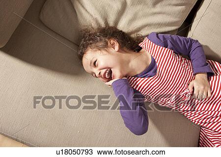 Stock Image - Little girl lying on couch laughing. Fotosearch