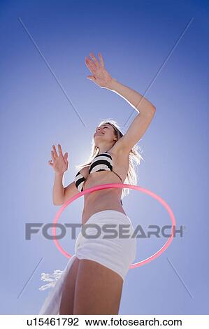 Stock Image - Low angle view of woman hula hooping. Fotosearch