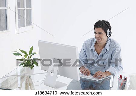Stock Image - Man at computer with headphones on. Fotosearch