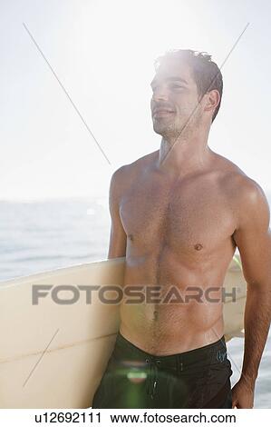 Stock Image - Man carrying surfboard out of water. Fotosearch