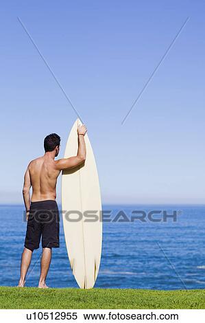 Stock Photography - Man holding surfboard by ocean. Fotosearch