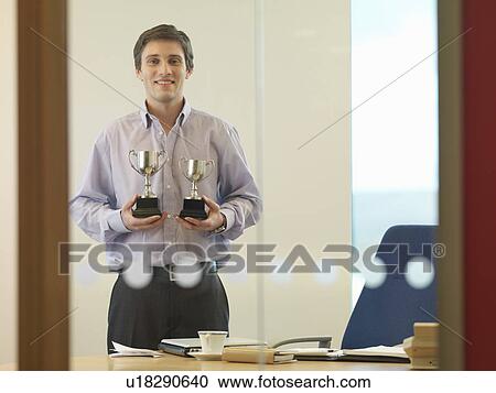 Stock Image - Man holding trophies. Fotosearch