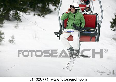 Stock Image - Man in Chairlift with Cellphone. Fotosearch
