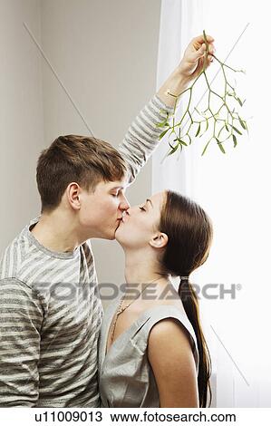 Stock Image - Man kissing woman while holding mistleto. Fotosearch