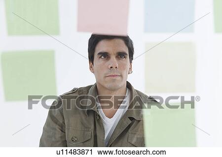 Stock Image - Man looking at different coloured post-it notes. Fotosearch