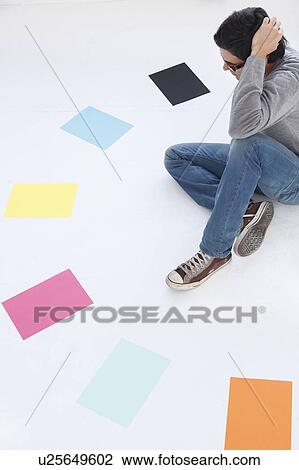 Stock Image - Man looking at different coloured paper, white background. Fotosearch