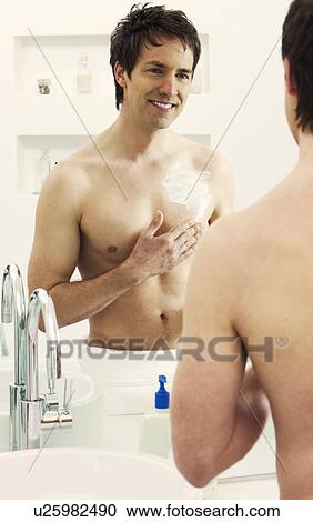 Stock Image - Man moisturizing chest in bathroom. Fotosearch