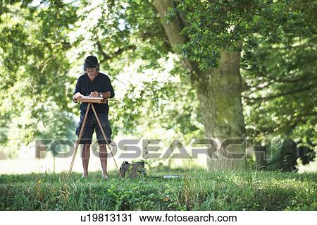 Stock Image - Man painting a picture in a park. Fotosearch