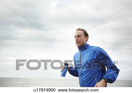 Stock Image - Man running by the sea on cloudy day. Fotosearch