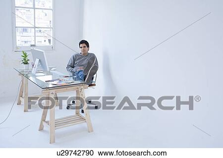 Stock Image - Man sitting at computer with his feet up. Fotosearch