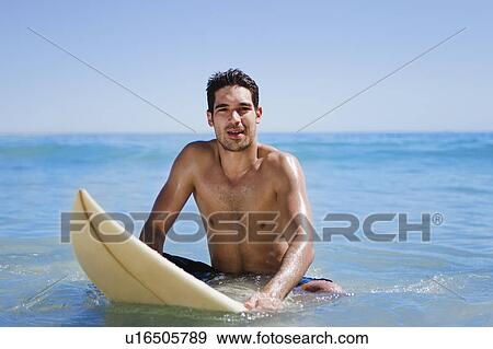 Stock Photo - Man sitting on surfboard in water. Fotosearch