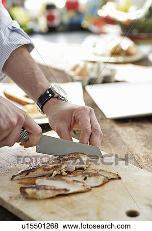 Stock Photo - Man slicing chicken on cutting board. Fotosearch